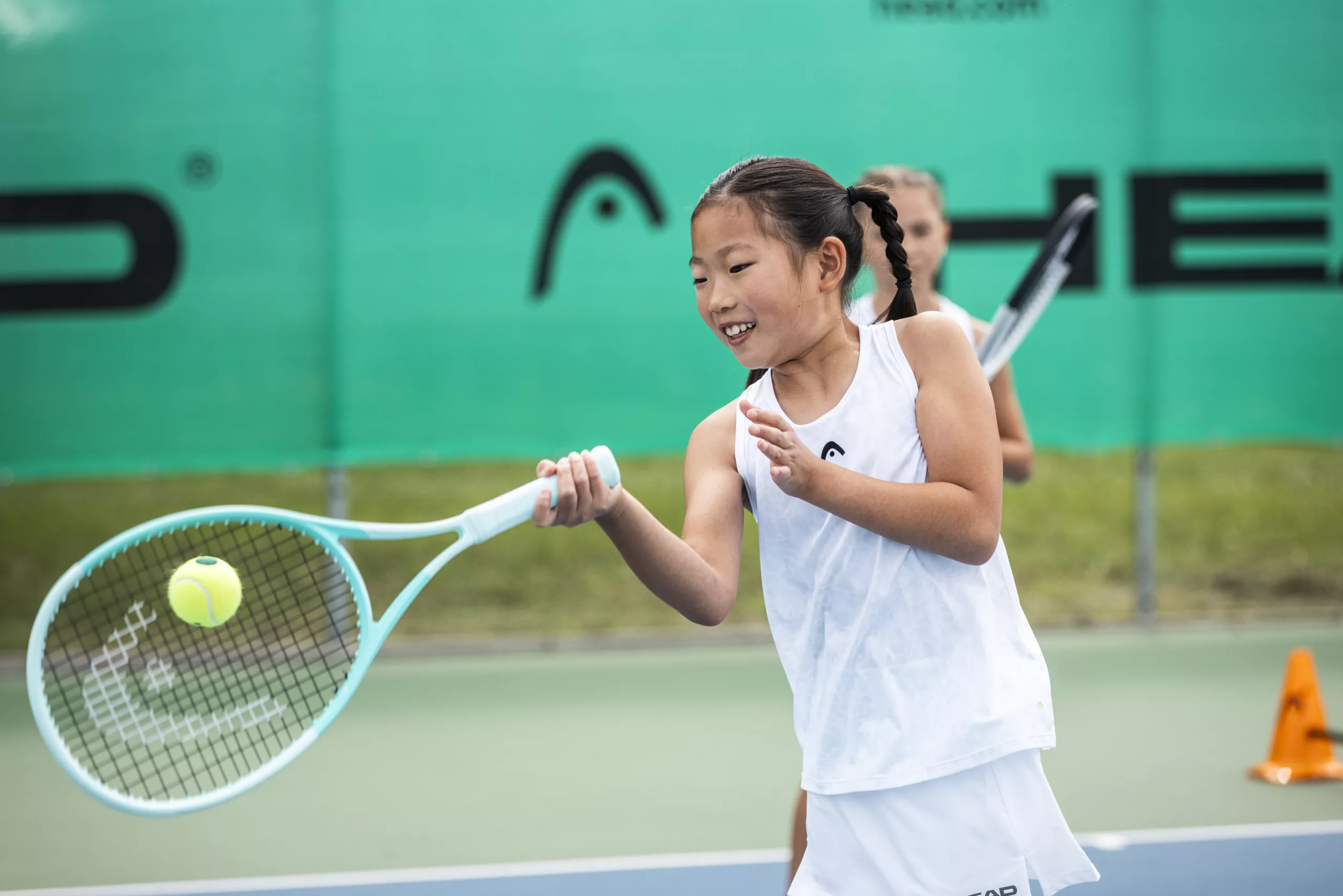Young girl hitting a tennis ball with a HEAD tennis racket.