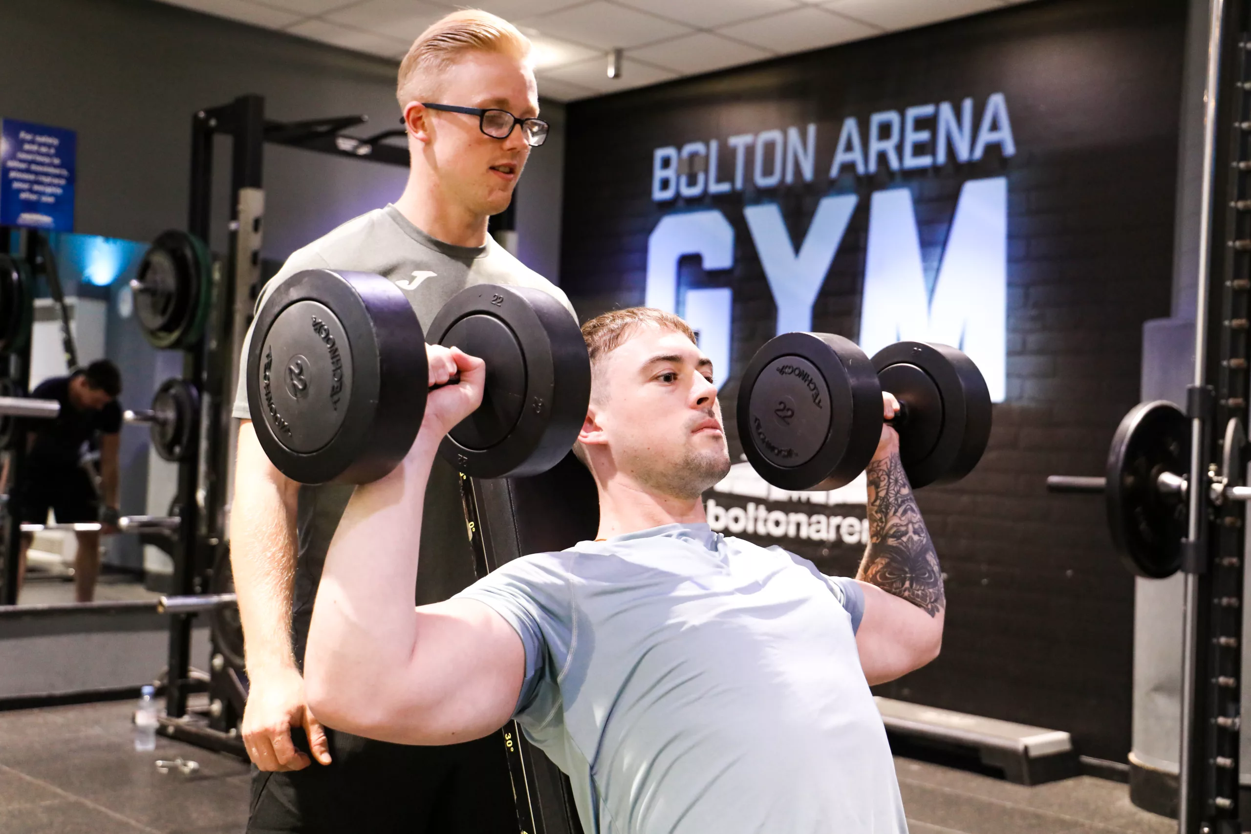 Man being spotted by a friend in the gym weights section of Bolton Arena