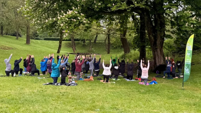 A large group of people doing yoga at Queens Park in Bolton.