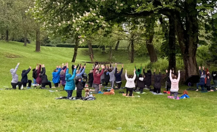 A large group of people doing yoga at Queens Park in Bolton.