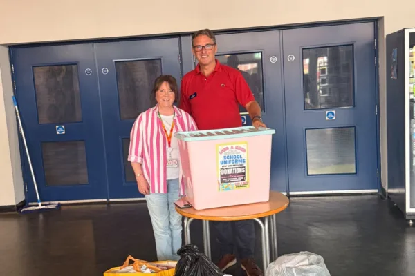 man and woman stood next to collection box of donated school uniform and stationary.